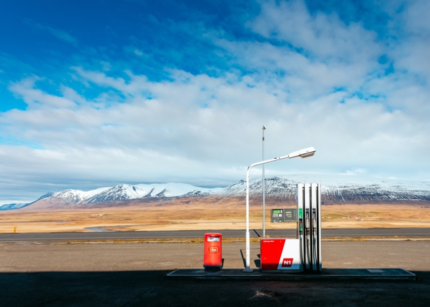 A single fuel pump with a blue sky and clouds above the mountains in the background.