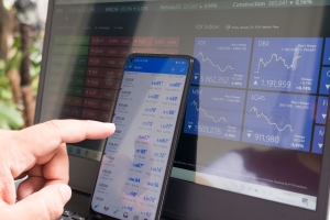 smart phone in front of computer screen with market and hedging information on the screens