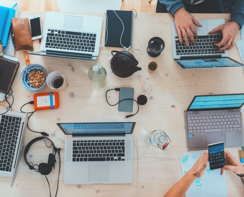 view from above of meeting table with laptops and arms visible; soft skills