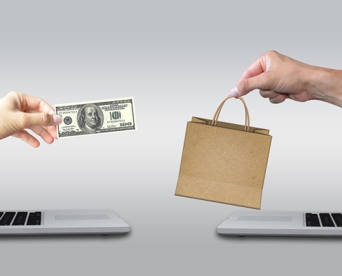 Hands reaching toward each other from laptops. One holding money, the other holding a bag. purchasing carbon credits