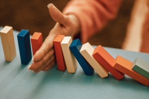 line of colored dominos falling with a hand stopping the fall; hedging - identifying risks