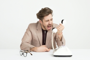 image of man sitting at desk, yelling into a phone receiver; soft skills matter: communication