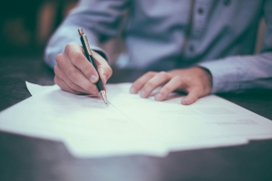 image of hands holding a pen, appears to be writing on a document on a table