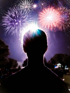 silhouette of an adult head in foreground, colorful fireworks in background against night sky; 4th of July