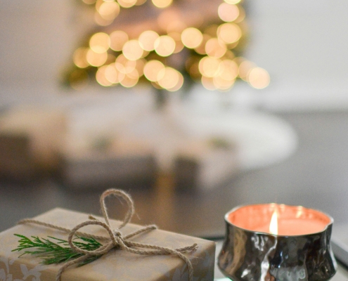 picture of wrapped present next to a candle in foreground, blurry picture of Christmas tree in background; time with family at Christmas