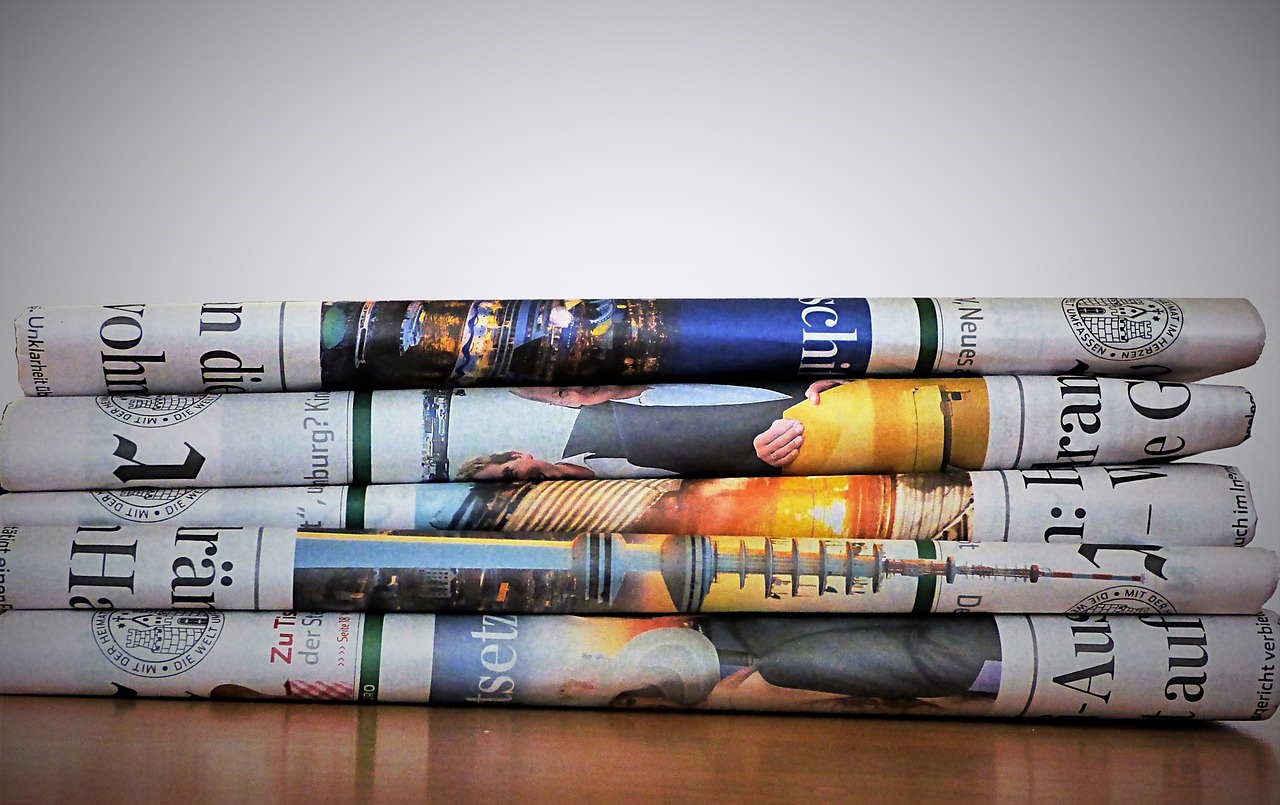 stack of folded newspapers on brown table against white background; current events