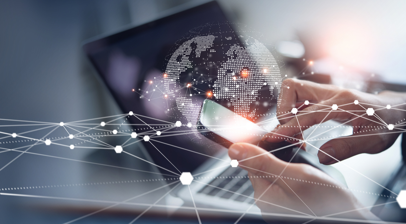 image of hands holding a smart phone in front of an open laptop with images of interconnected dots and lines over the top and a transparent image of a globe in the background